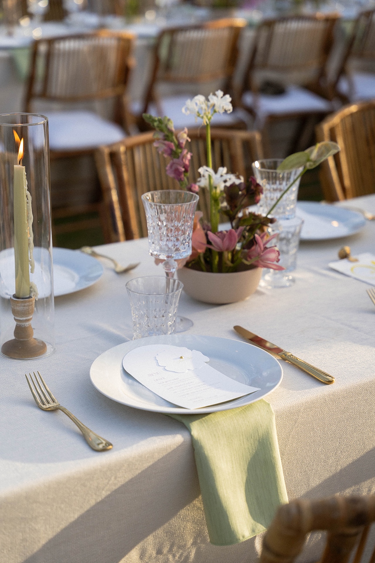 Close-up of a reception place setting with a menu card, green napkin, and soft floral arrangement.