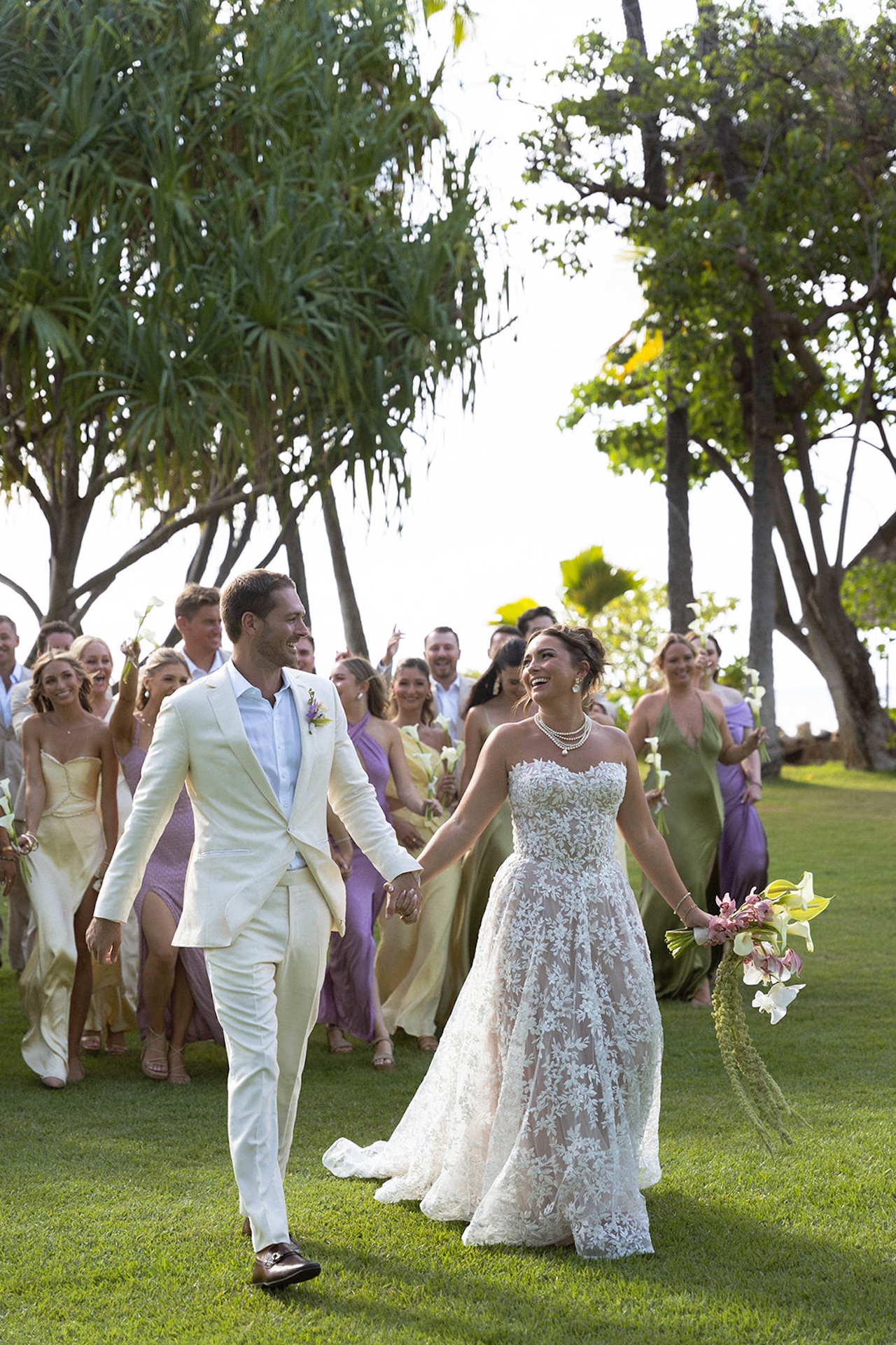 Guests cheer as the couple walks up the lawn during their Lanikuhonua wedding celebration.