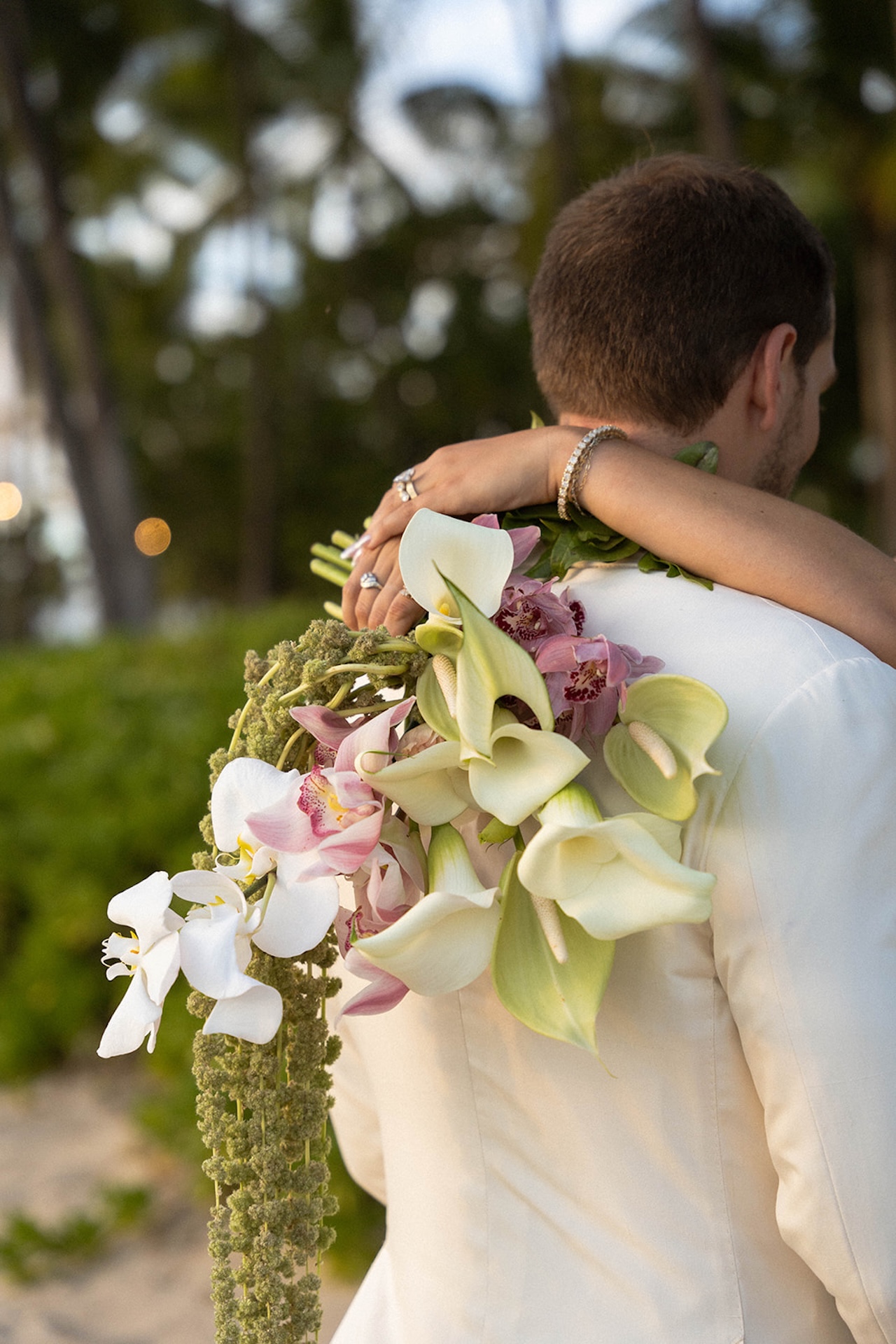 Close-up of the bride’s arms around the groom with tropical orchids cascading over his shoulder.