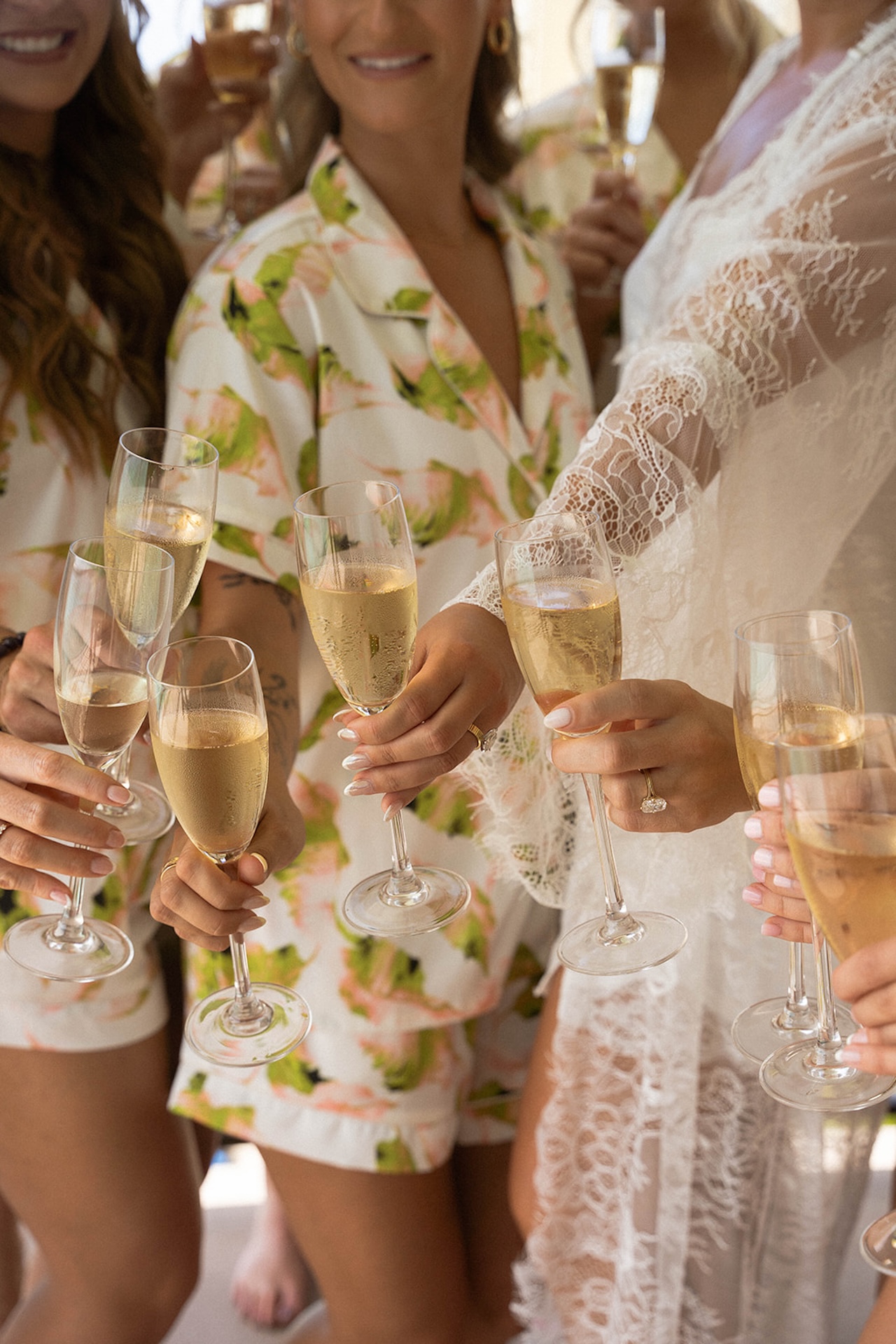 Bridesmaids in matching floral pajamas raise champagne glasses together.