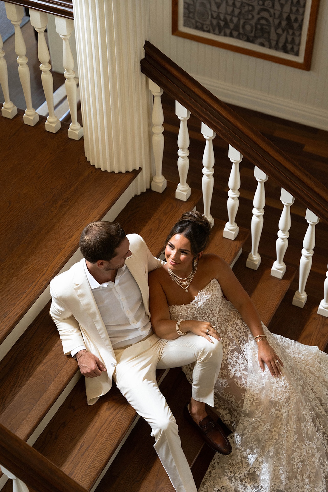 The bride and groom sit together on the stairs, smiling during their Lanikuhonua wedding day.