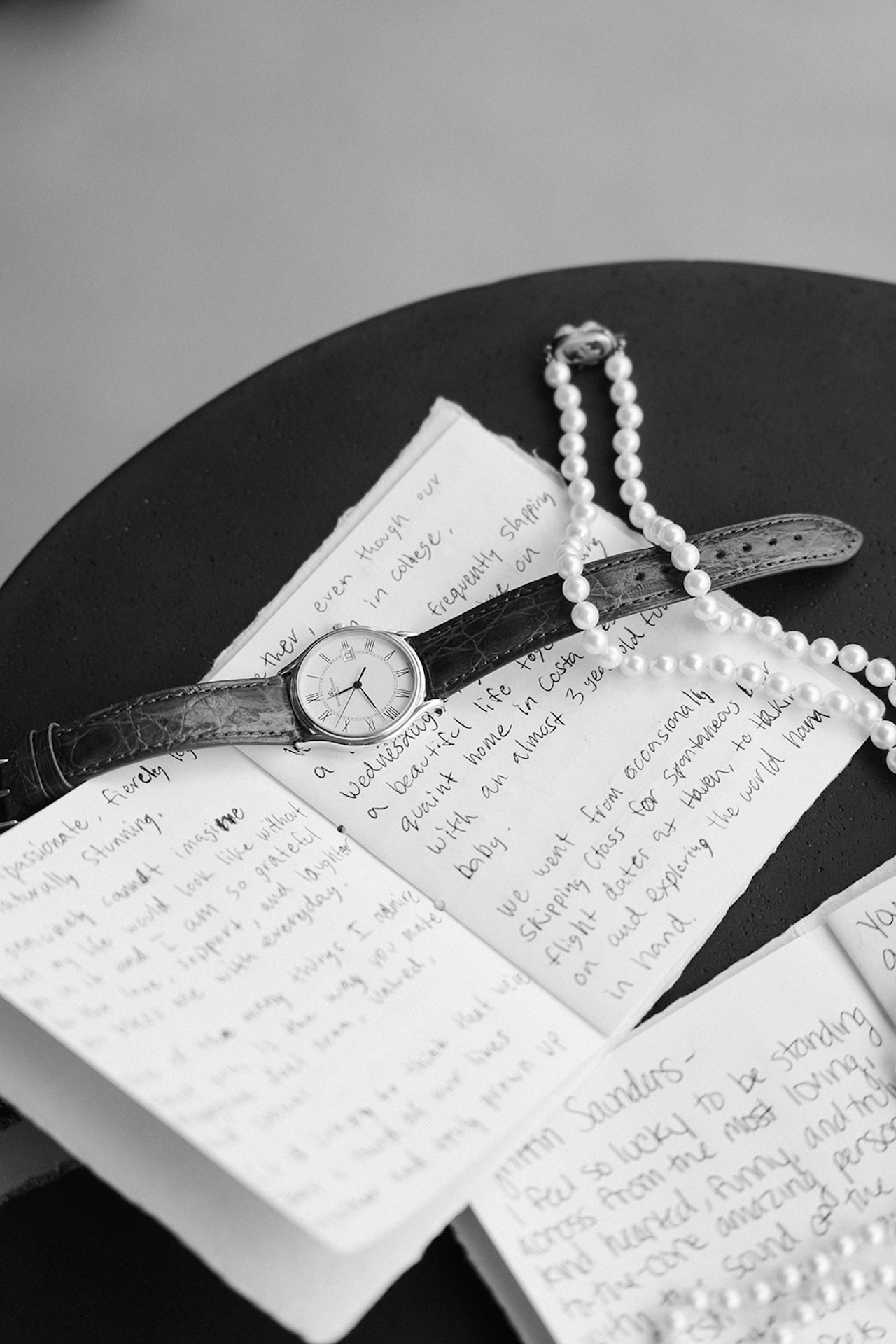 Close-up of handwritten vows, a watch, and pearl jewelry laid out together.