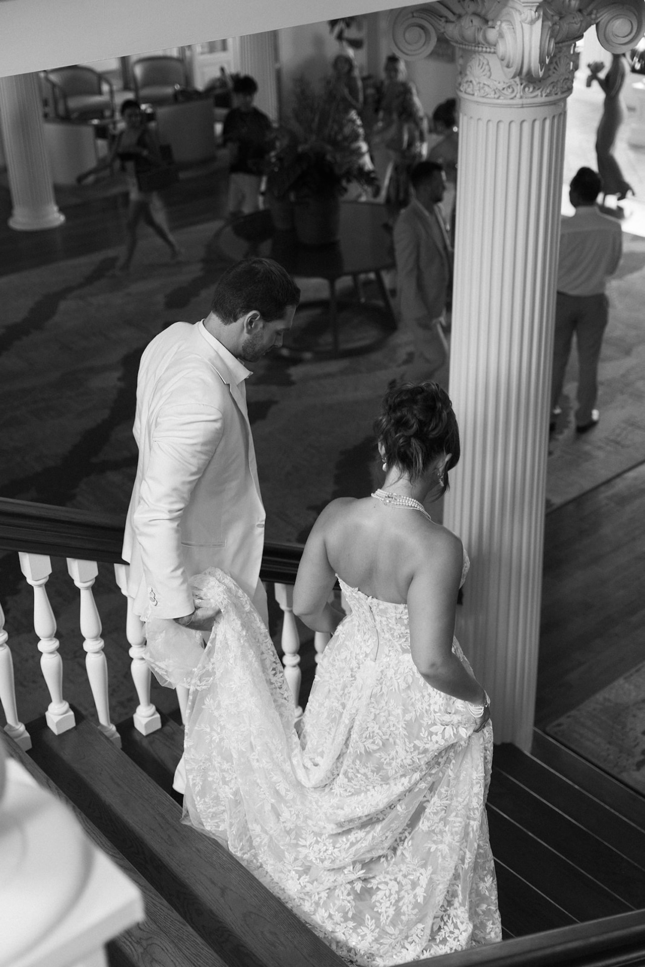 A black and white image of the bride and groom walking down old wooden stairs as the groom holds the brides train.