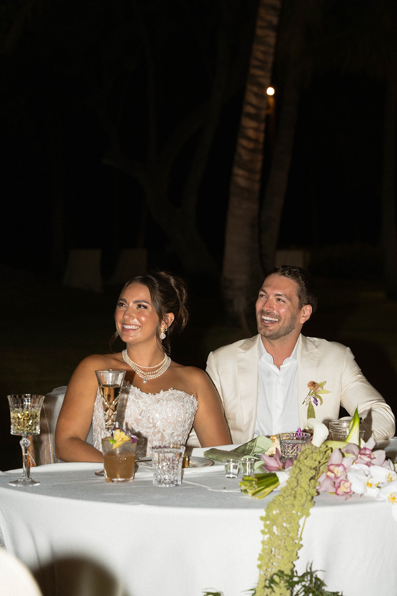 The bride and groom smile warmly during a toast at their Lanikuhonua wedding dinner.