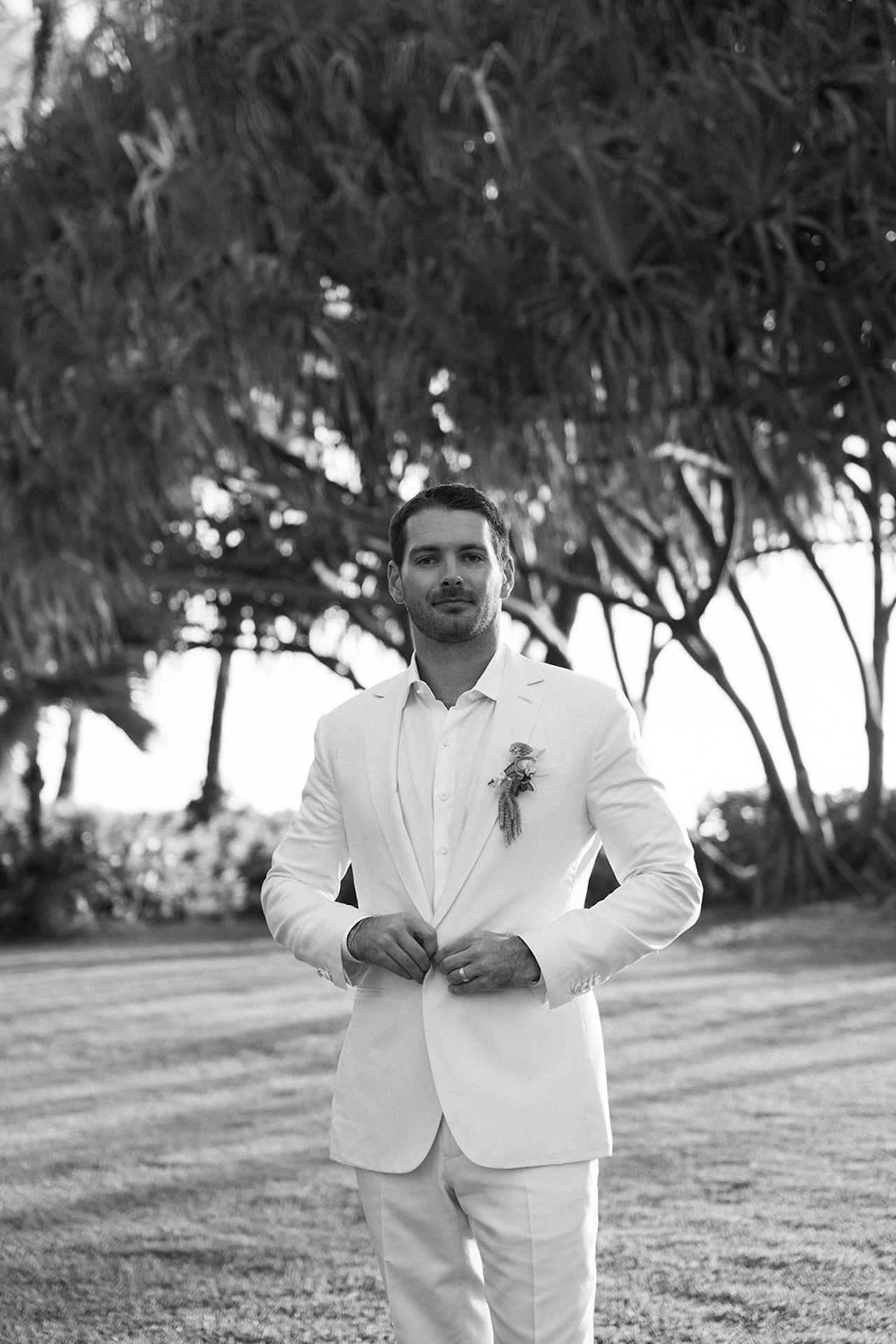Black-and-white portrait of the groom standing in a white suit during his Lanikuhonua wedding.
