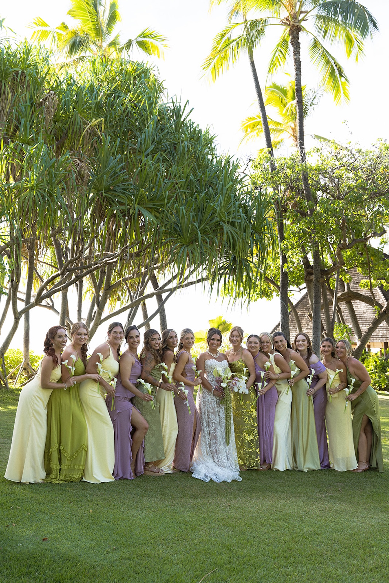 The bride poses with her bridesmaids wearing pastel dresses under the palm trees.