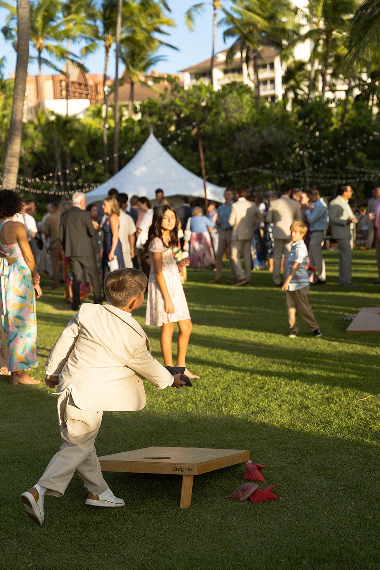 Kids playing cornhole on the lawn while the wedding guests drink and visit during cocktail hour.