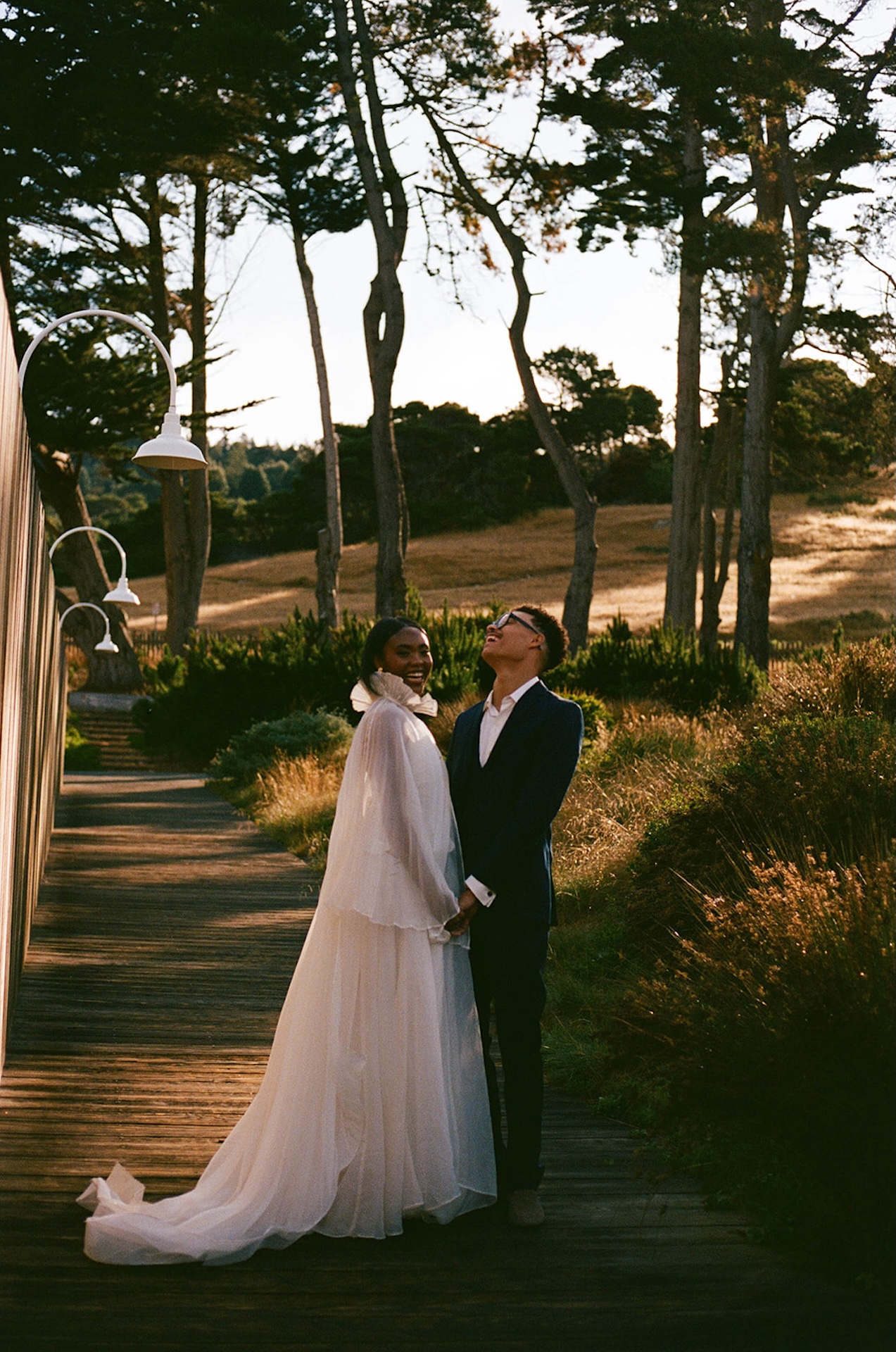 A film photo of the bride and groom laughing and standing together while holding hands on a wooded path during their Sea Ranch Lodge Wedding
