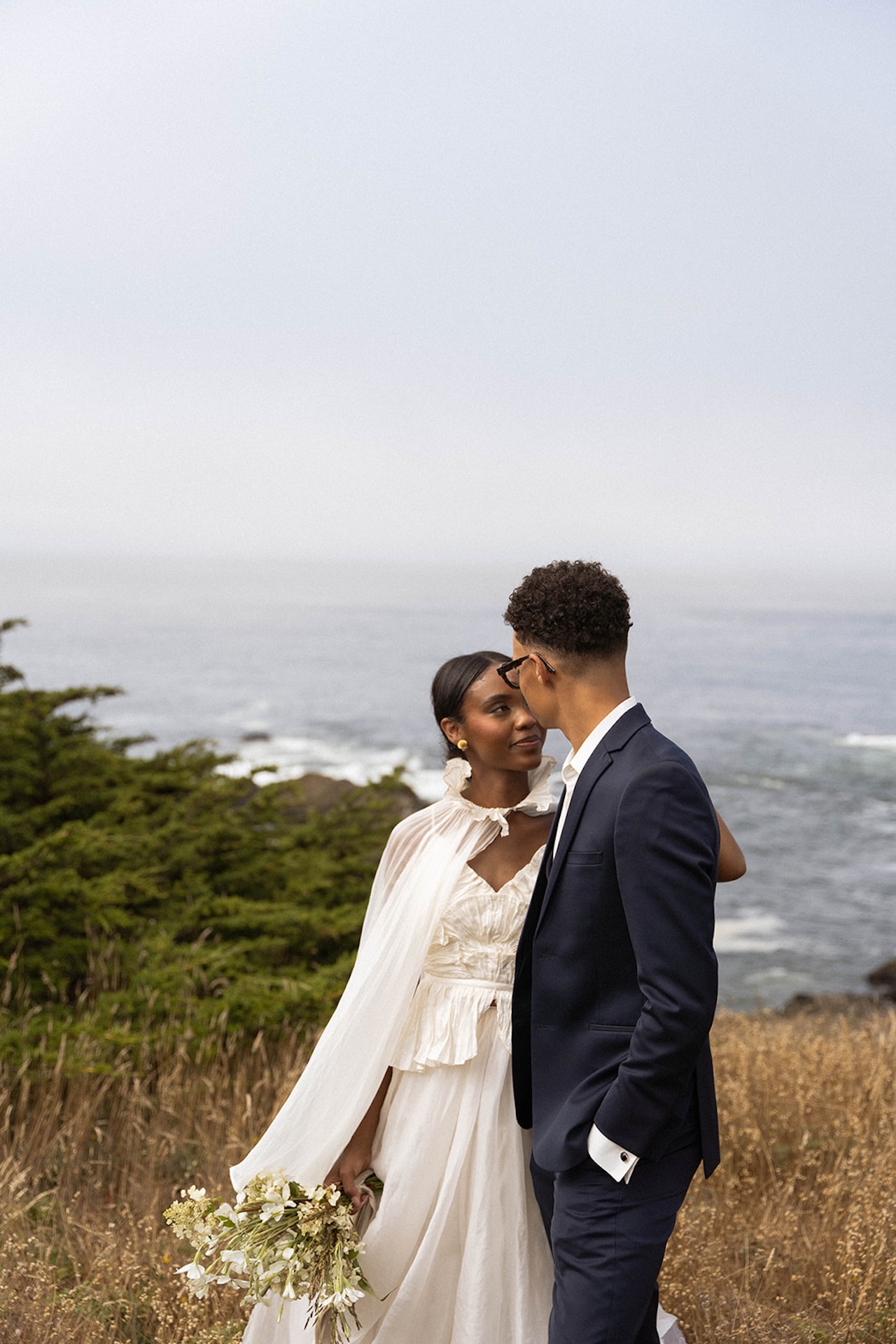 The bride and groom hugging each other close and looking at each other with the California coast in the background.