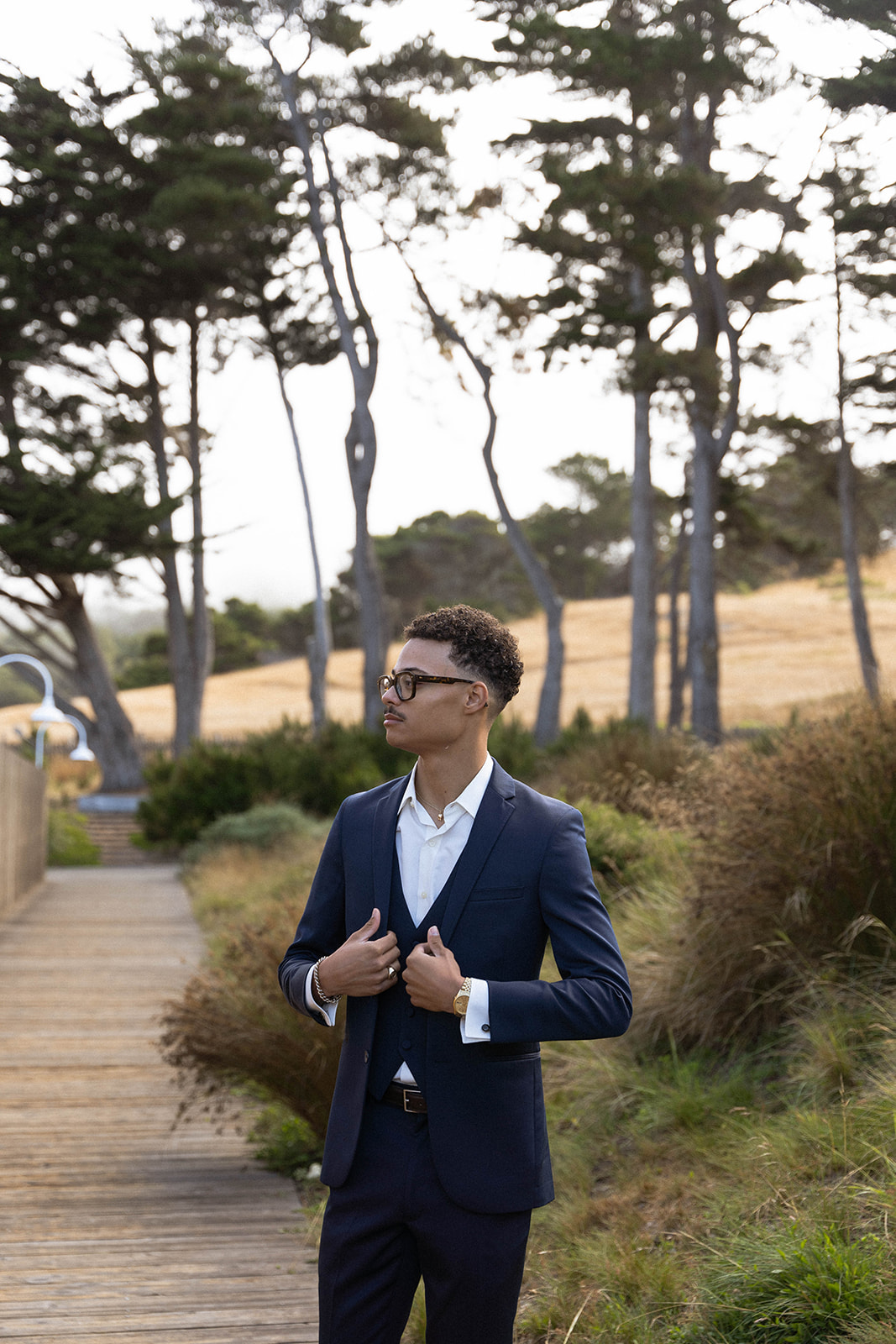 The groom standing on a wooden path with trees in the background as he adjusts his suit jacket at his Sea Ranch Lodge Wedding
