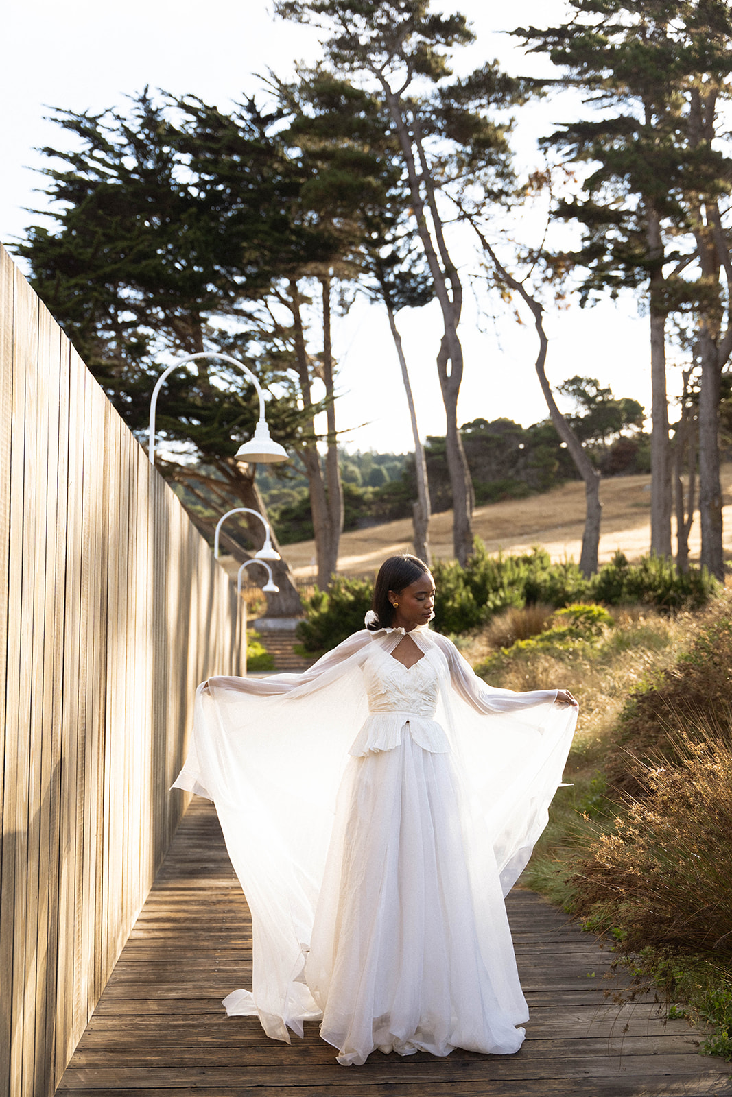 The bride holding her hands out with her veil trailing behind her on a wooden path at her Sea Ranch Lodge Wedding
