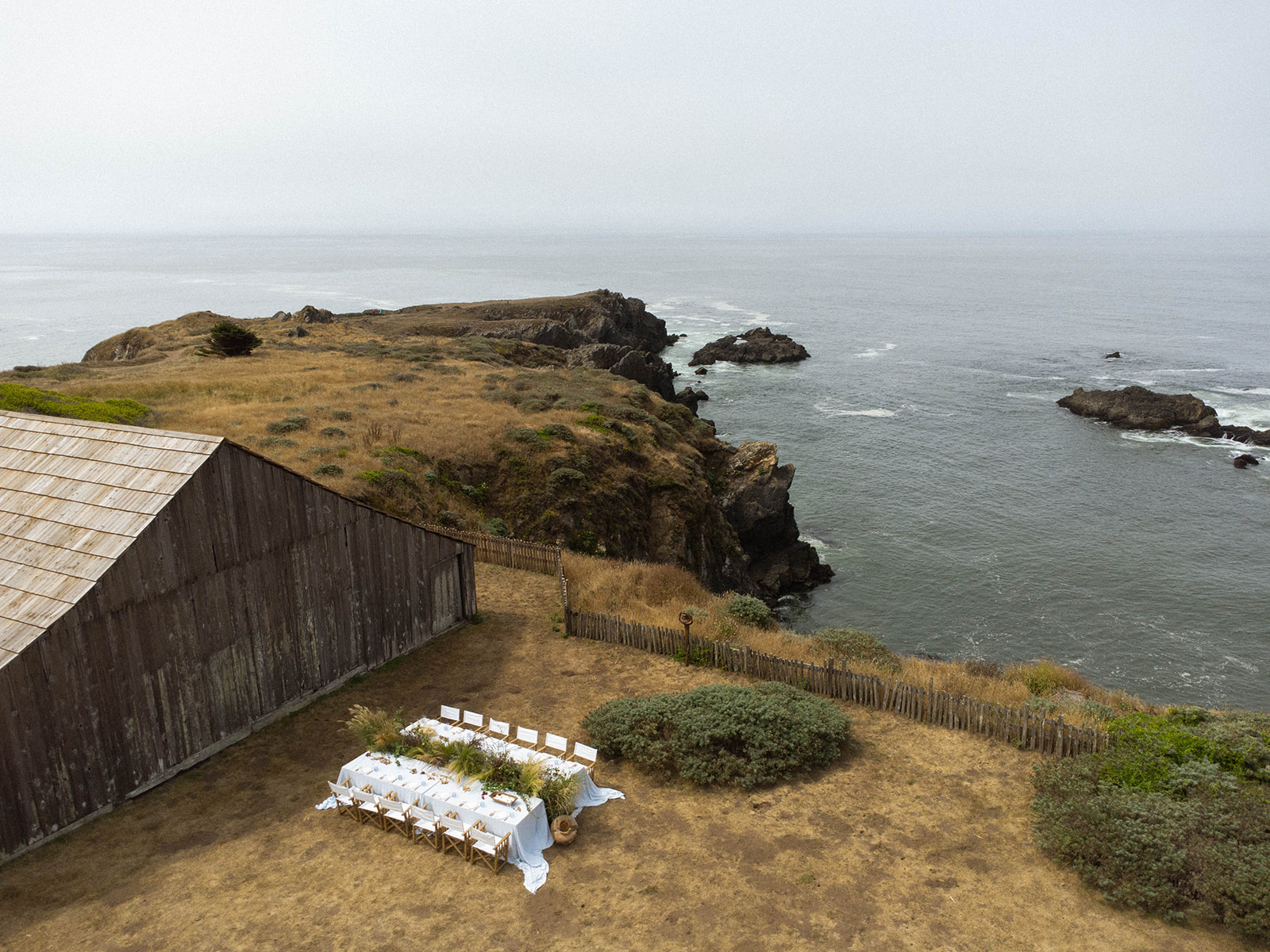 A drone view of a barn and a wedding reception table overlooking the cliff coastline for a Sea Ranch Lodge Wedding
