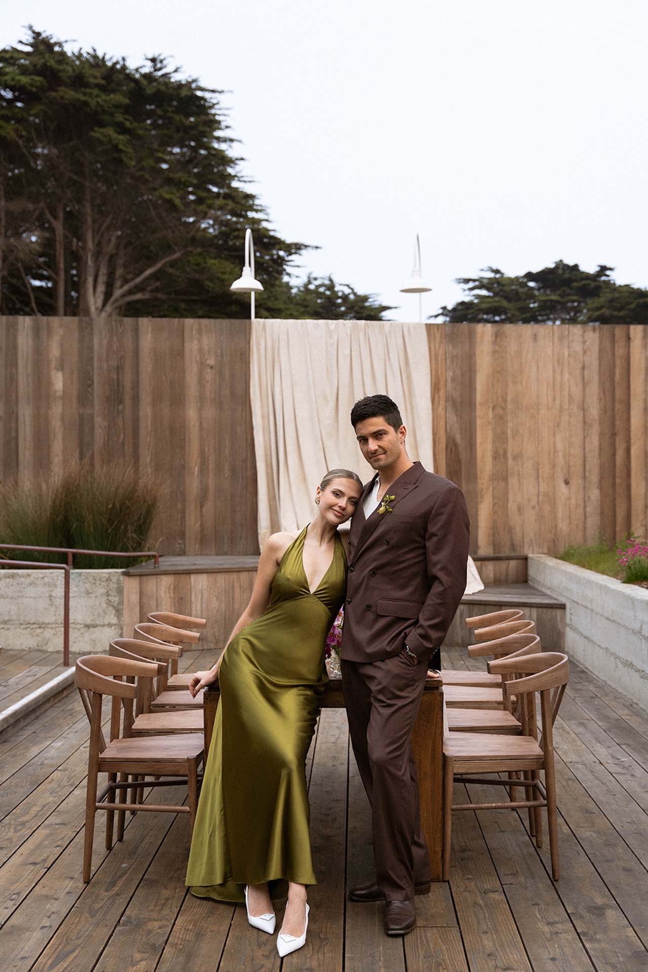 Bride and groom leaning against a wooden recpetion table