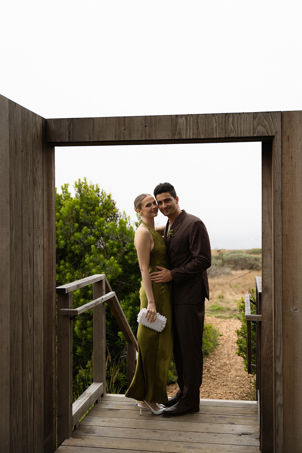 Bride and groom hugging on the top of the stairs of a wooden arch way while planning a destination wedding