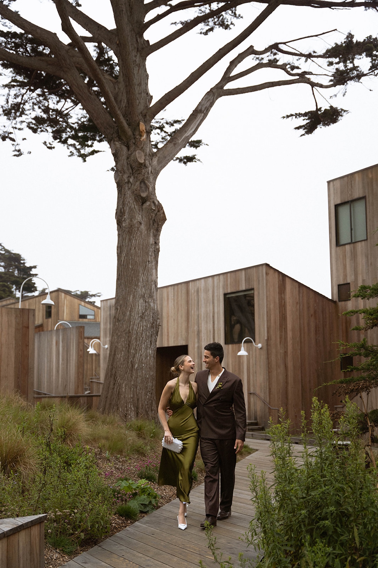 Bride and groom walking hand in hand past modern wooden cabins, reflecting intentional design choices made when planning a destination wedding.