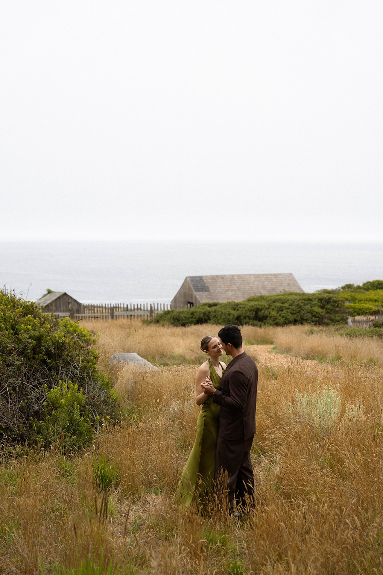Bride and groom dancing quietly in a grassy coastal landscape, embracing simplicity and presence when planning a destination wedding.