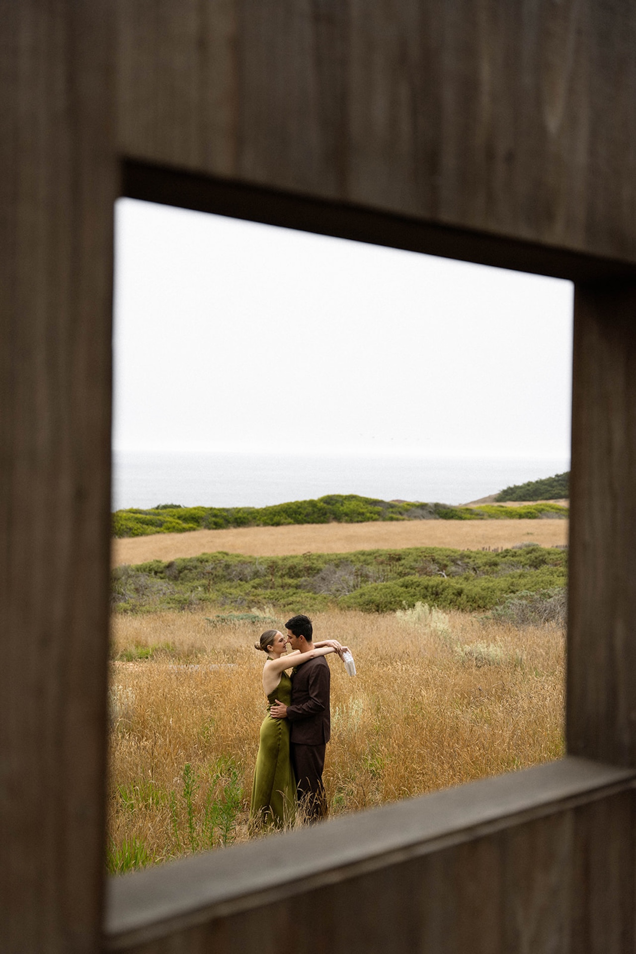 Framed view of the couple kissing through a wooden structure, creating depth and intentional composition.