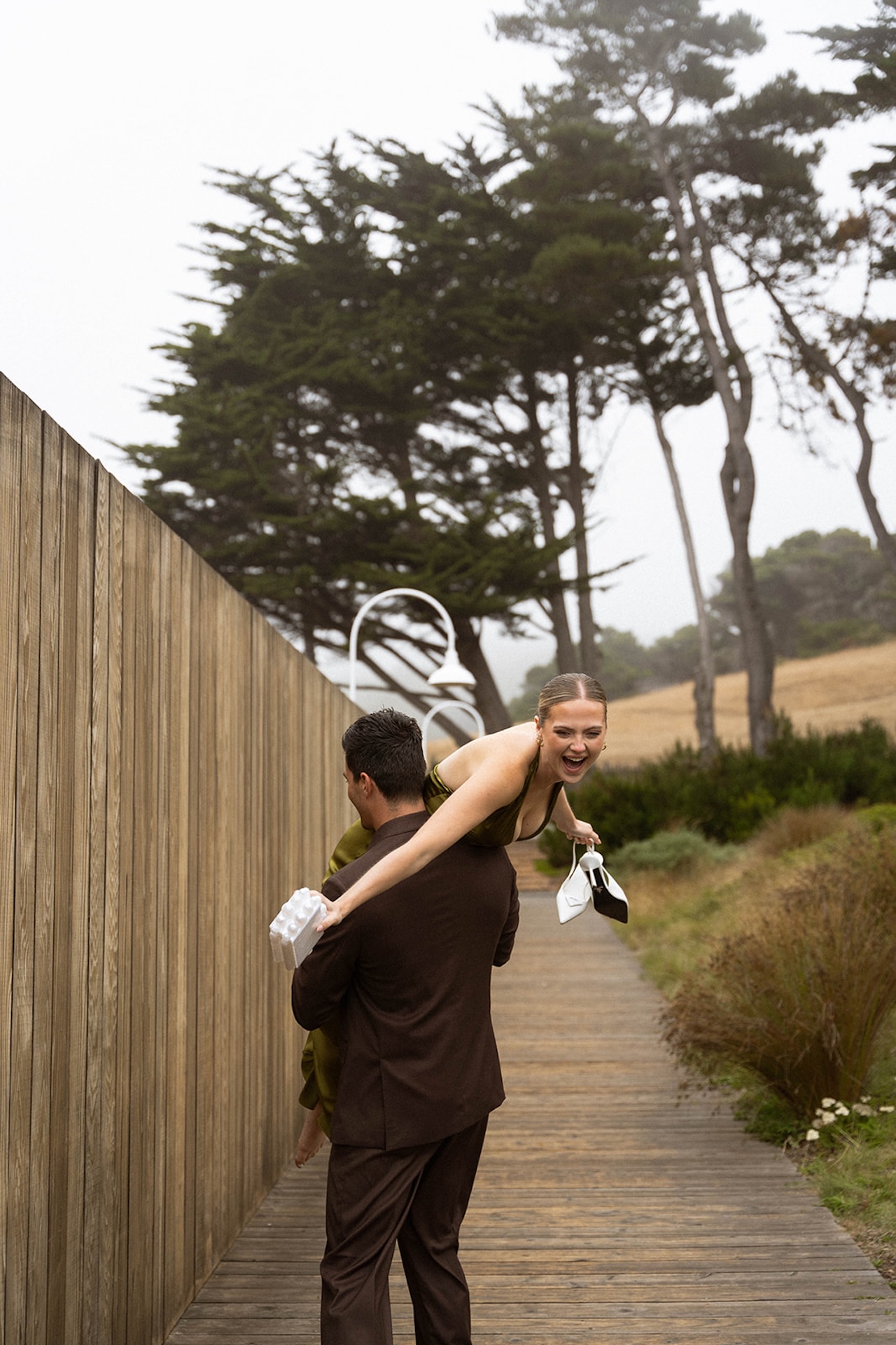 Bride laughing while being carried by the groom along a wooden boardwalk, capturing carefree movement and joy while planning a destination wedding.