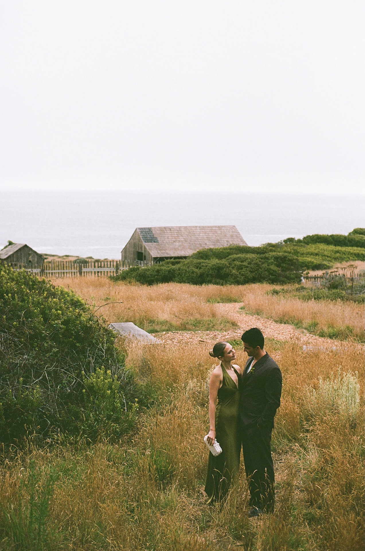 Bride and groom standing close in a coastal meadow with the ocean behind them, reflecting presence and simplicity while planning a destination wedding.