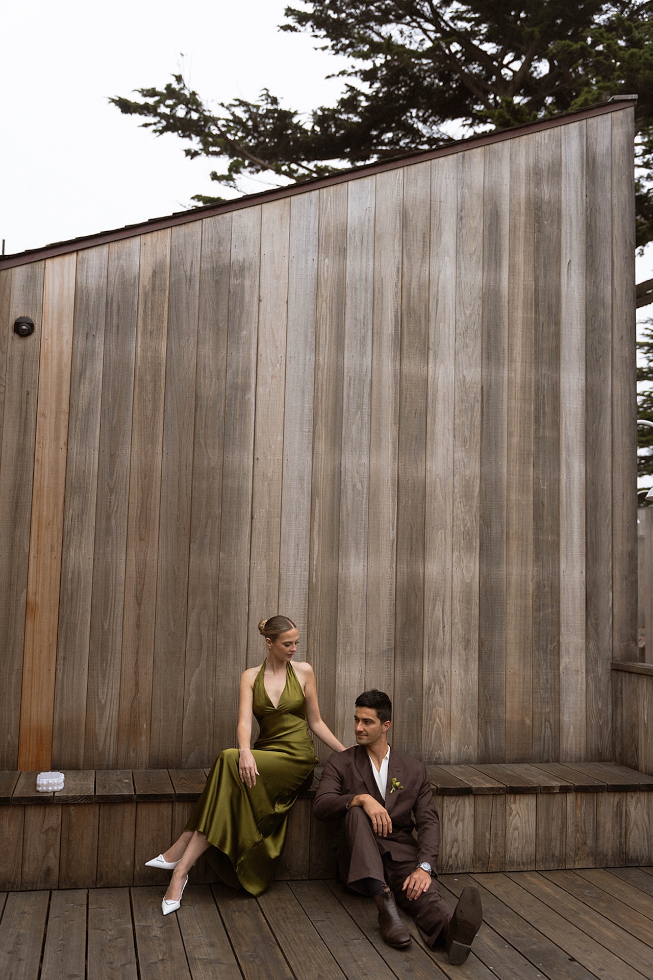 Minimalist portrait of the couple seated apart on a wooden platform, emphasizing clean lines and editorial wedding styling.