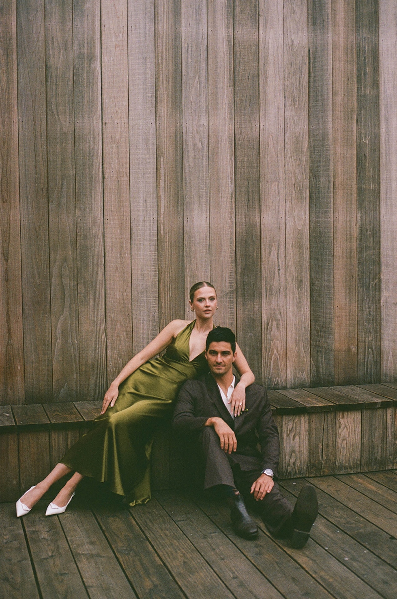Bride and groom seated against a weathered wood wall, styled in modern attire that reflects intentional design choices while planning a destination wedding.