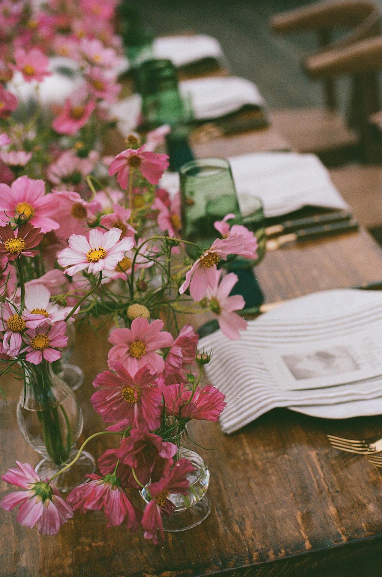 Detailed shot of pink florals in small glass vases alongside layered linens and tableware, reflecting curated details while planning a destination wedding.