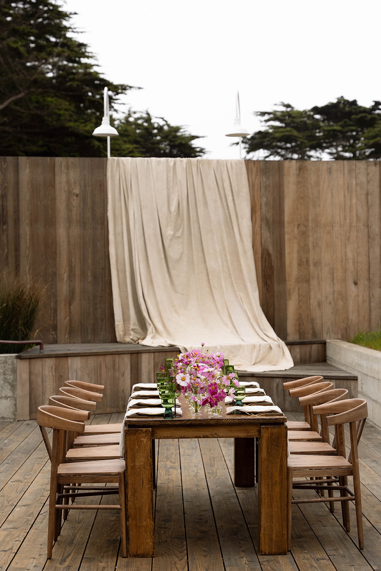 Symmetrical view of a wooden reception table framed by draped fabric and outdoor lighting, creating a calm and intentional atmosphere.