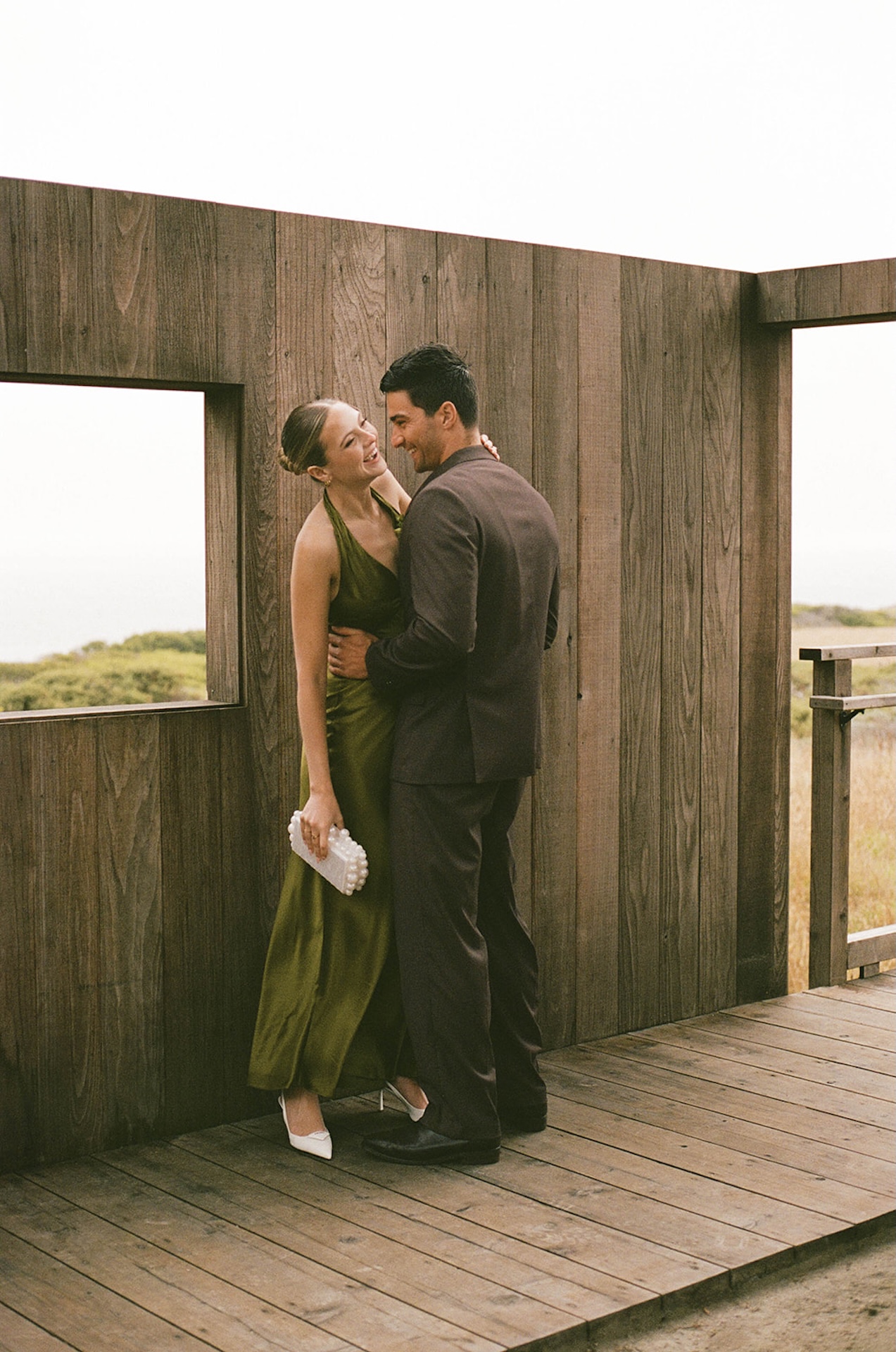 Bride and groom laughing as the groom carries the bride along a wooden path between modern cabins, ending the day with playful energy.