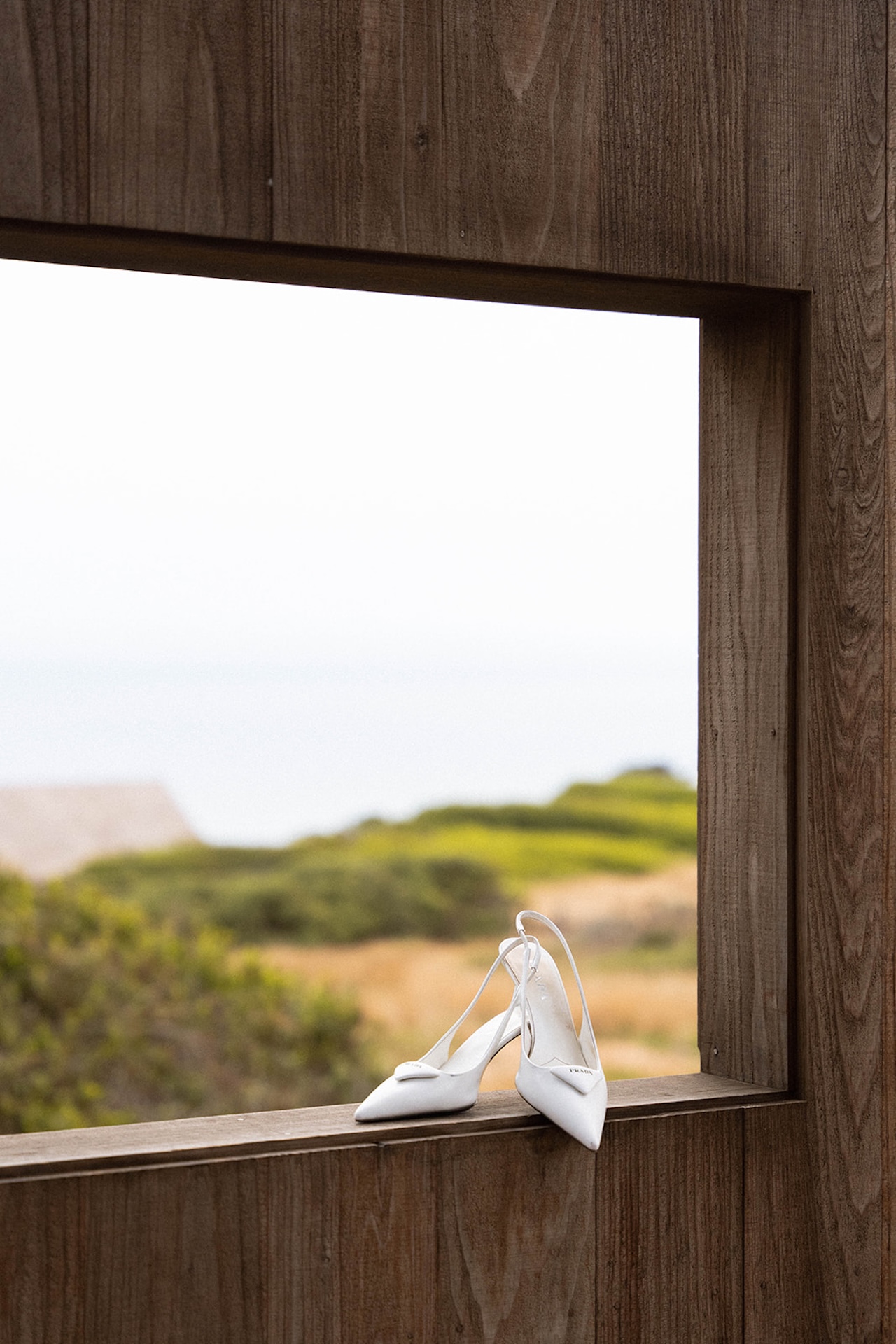 White bridal heels resting on a wooden window ledge overlooking coastal greenery, highlighting thoughtful details when planning a destination wedding.