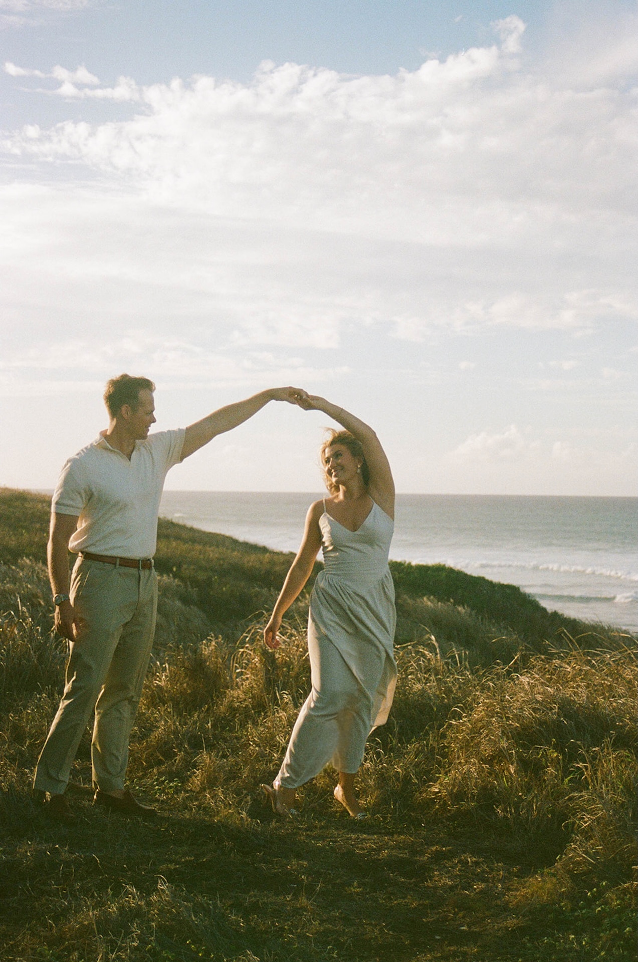 A twirling movement shot with the couple dancing together near the coastline, reflecting fun and natural ideas for engagement photos on oahu.