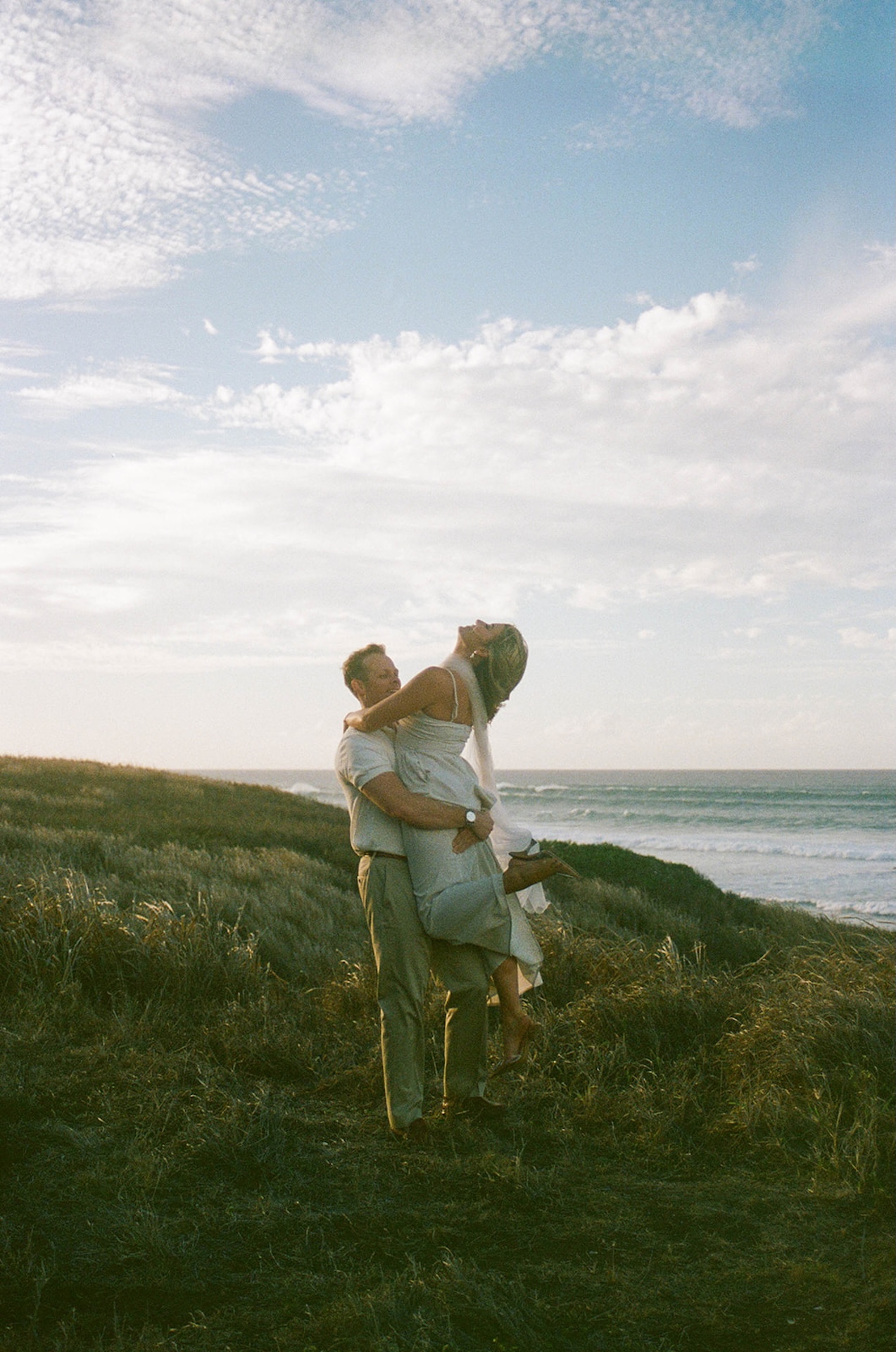 A playful lift during golden hour with the ocean behind them, capturing joyful, candid ideas for engagement photos.