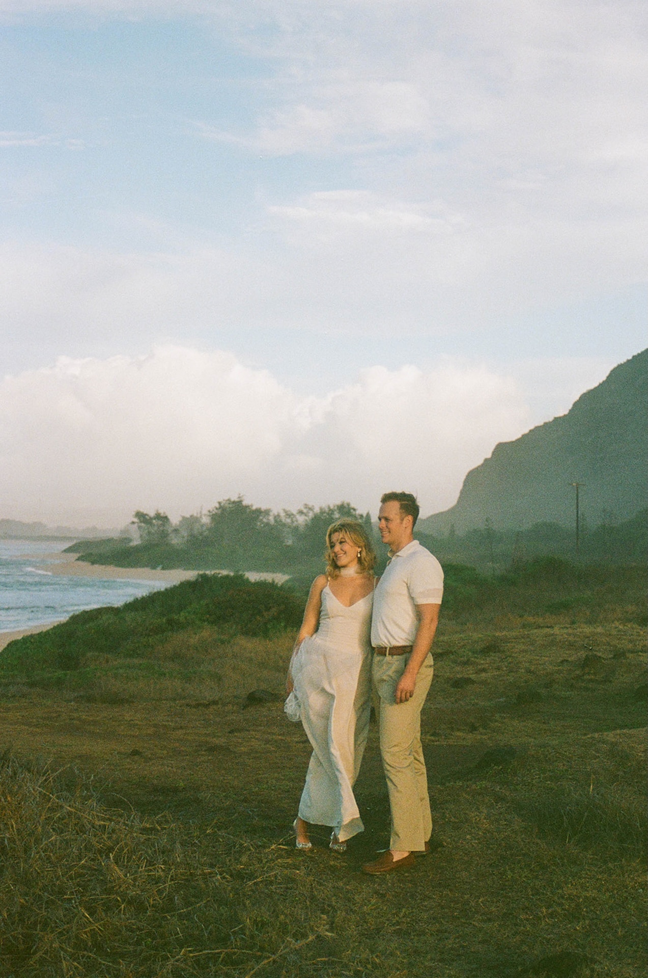 A wide scenic film photo of the couple standing together along the shoreline, featuring scenic and natural ideas for engagement photos on oahu.