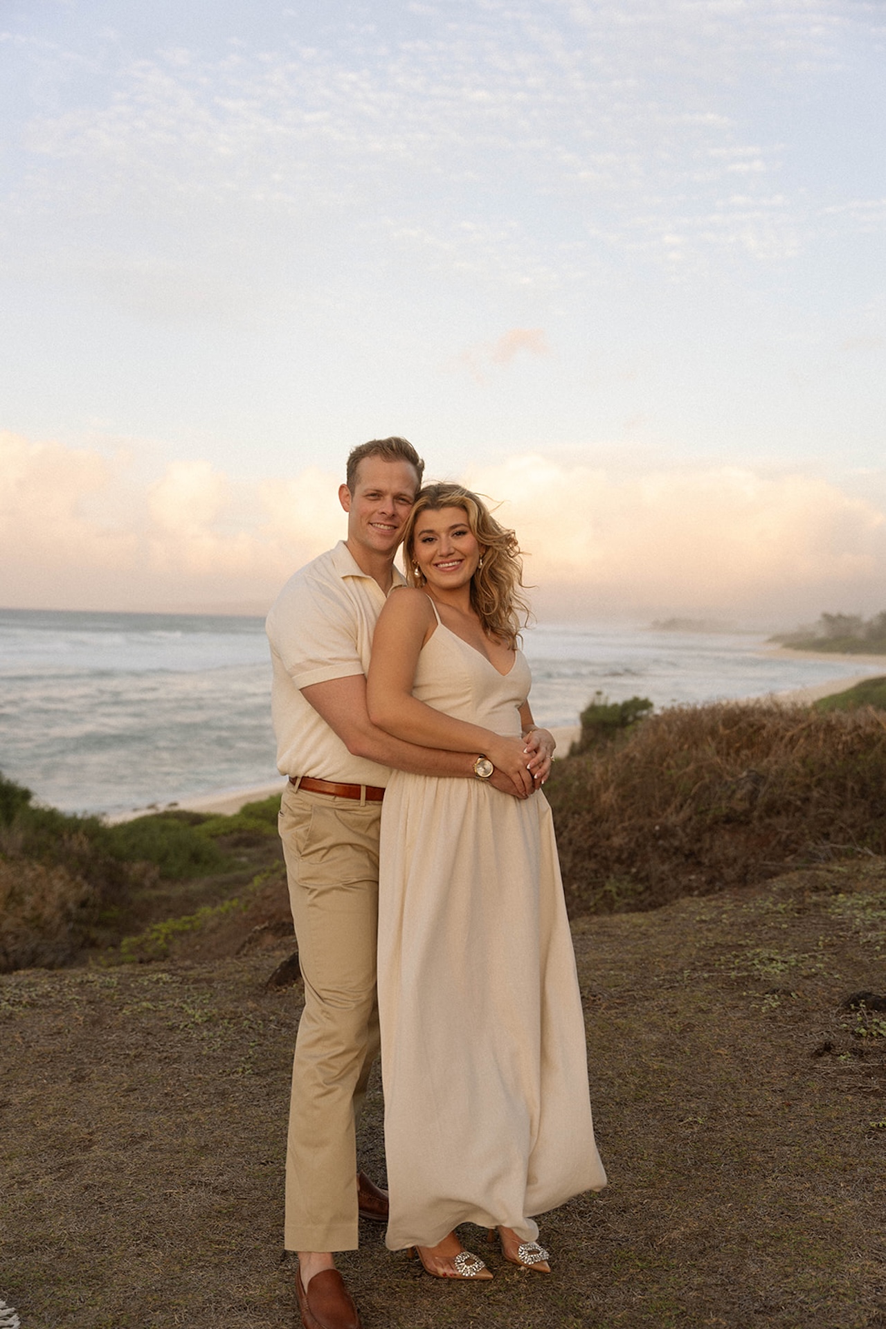 A smiling couple posing together with the ocean behind them, highlighting romantic and effortless ideas for engagement photos on oahu at sunset.