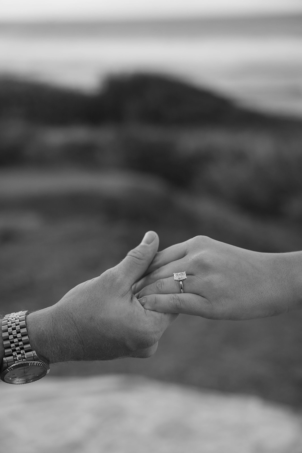 A black and white close-up of hands gently touching with an engagement ring in focus, emphasizing meaningful detail and connection.