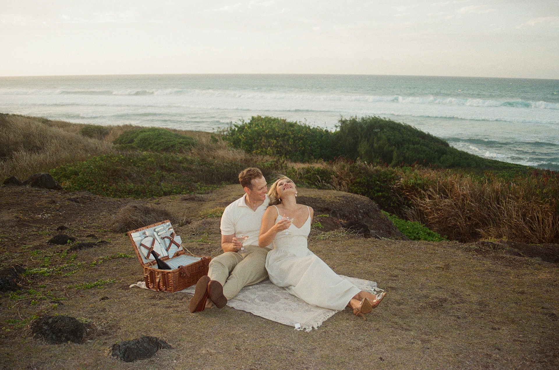 A wider picnic scene overlooking the ocean, featuring champagne, relaxed posing, and lifestyle-inspired ideas for engagement photos on oahu.