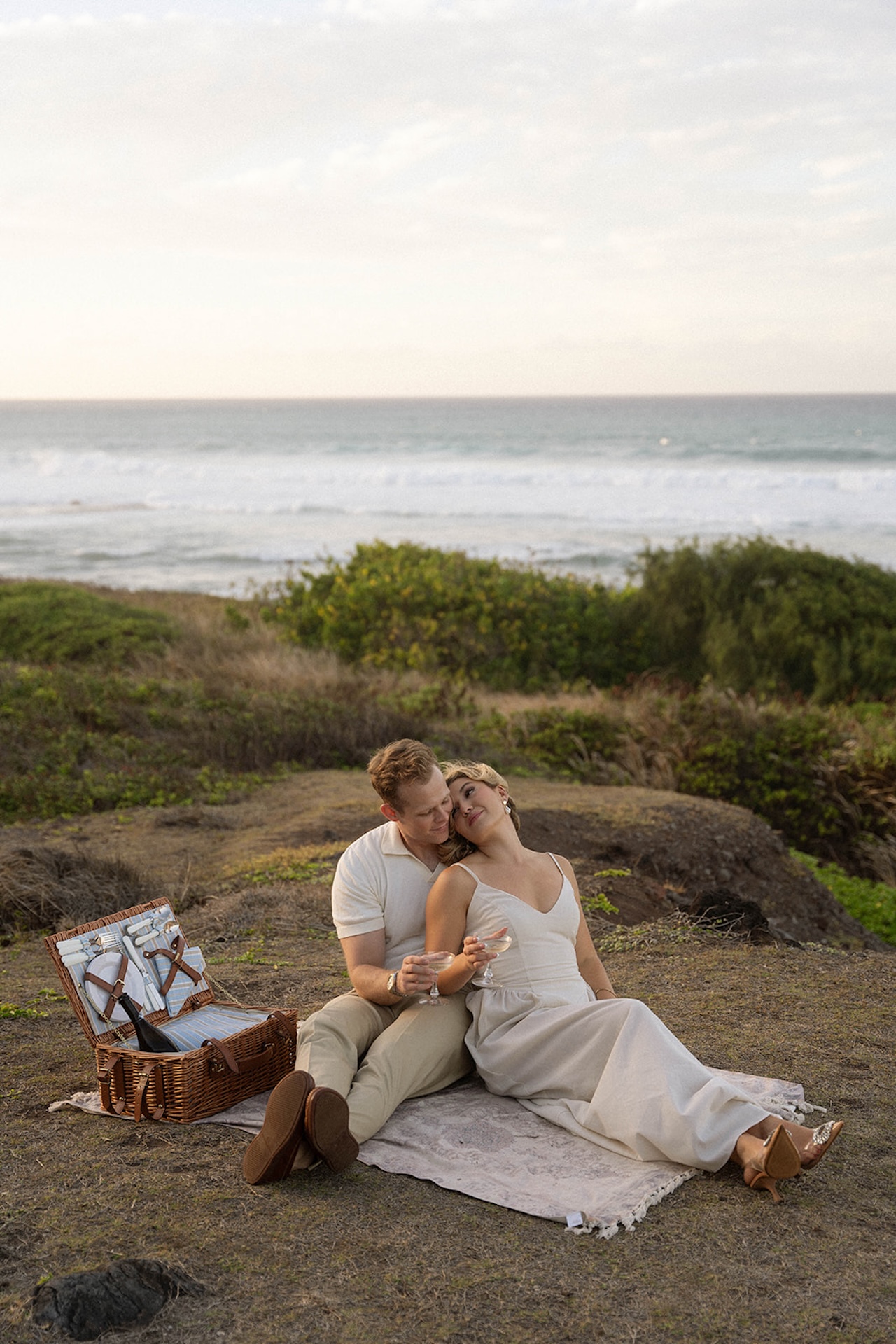 A relaxed picnic-style scene with the couple sitting on a blanket, champagne glasses in hand, showcasing lifestyle-inspired ideas for engagement photos on oahu.