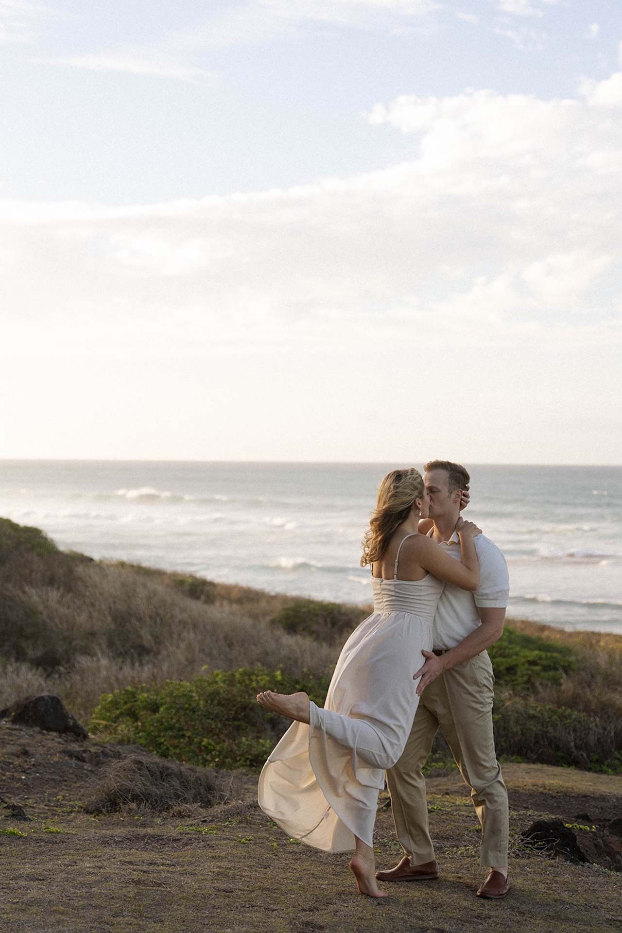 The couple standing and hugging her fiance along a coastal path, capturing movement-filled ideas for engagement photos on oahu with ocean views.