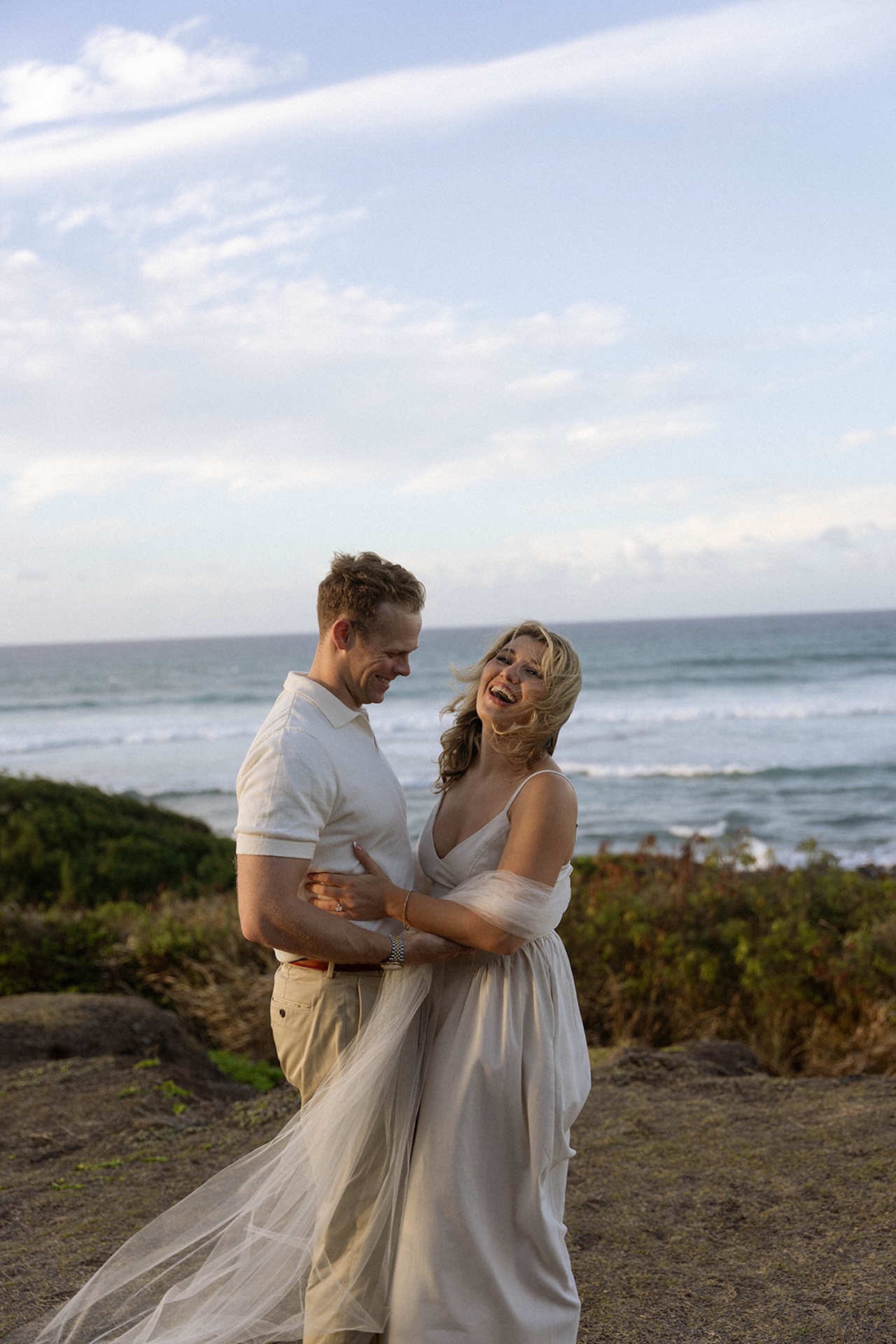 A joyful candid of the couple laughing together as the girls scarf flows in the breeze beside the shoreline.