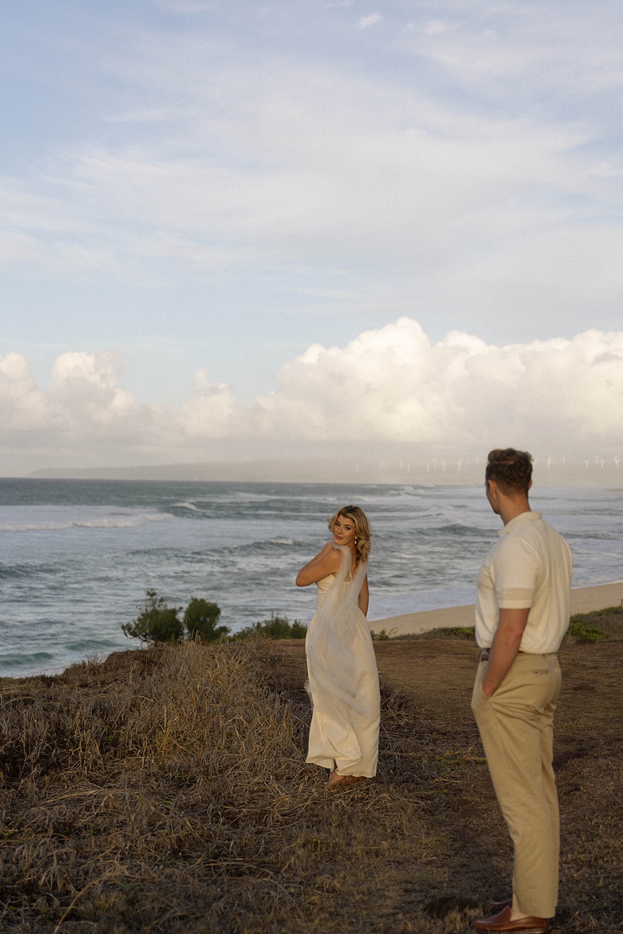 A wide scenic shot of the couple standing together along the shoreline, featuring scenic and natural ideas for engagement photos on oahu.
