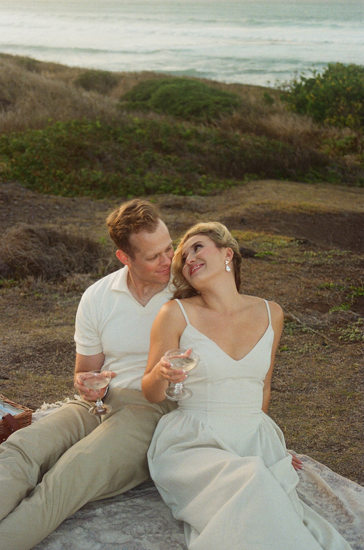 The couple sitting close together holding glasses, smiling and looking at each other, reflecting romantic ideas for engagement photos on oahu with a relaxed coastal vibe.