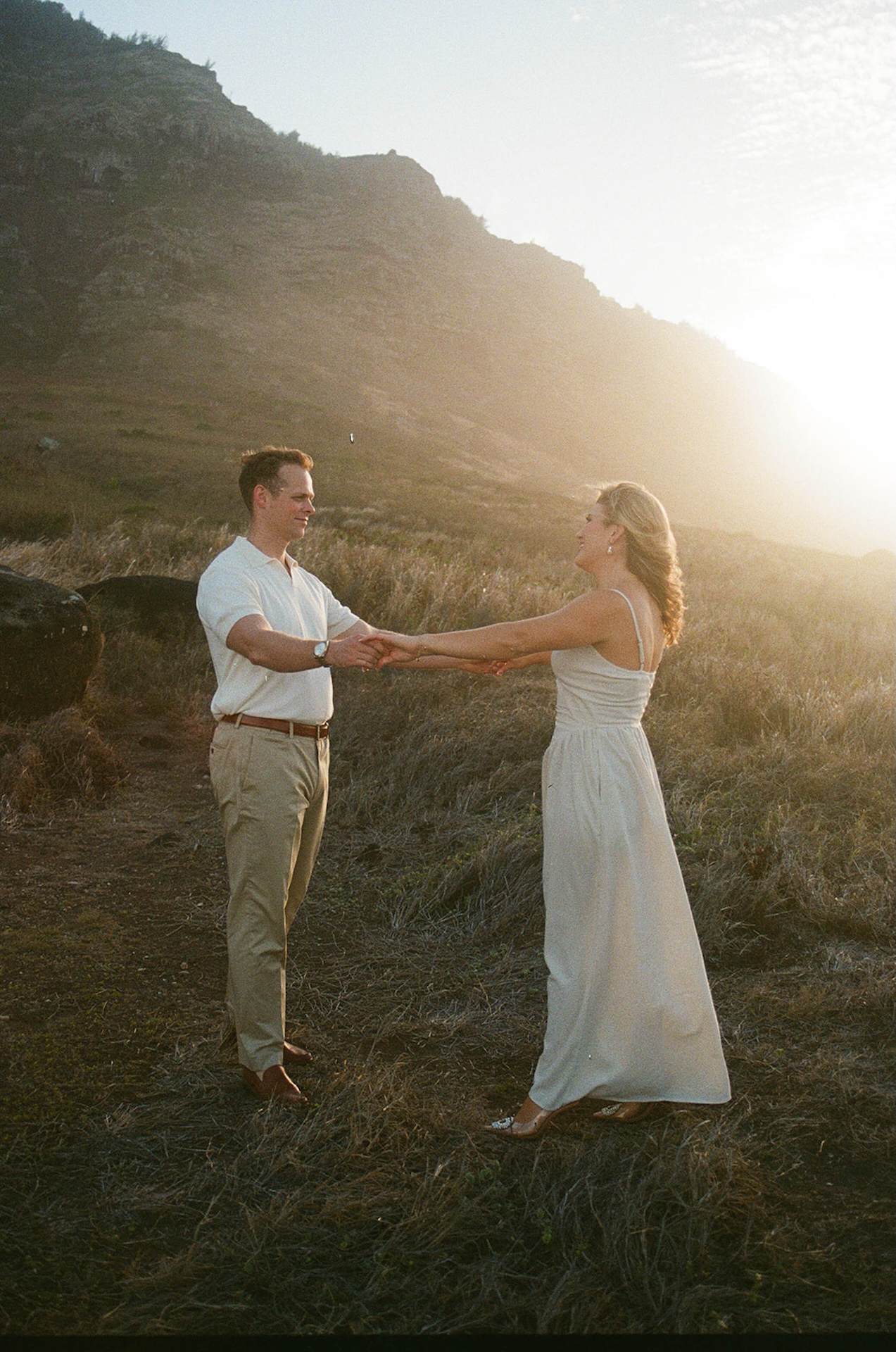 The couple holding hands while standing in an open coastal field at sunset, featuring cinematic ideas for engagement photos on oahu.