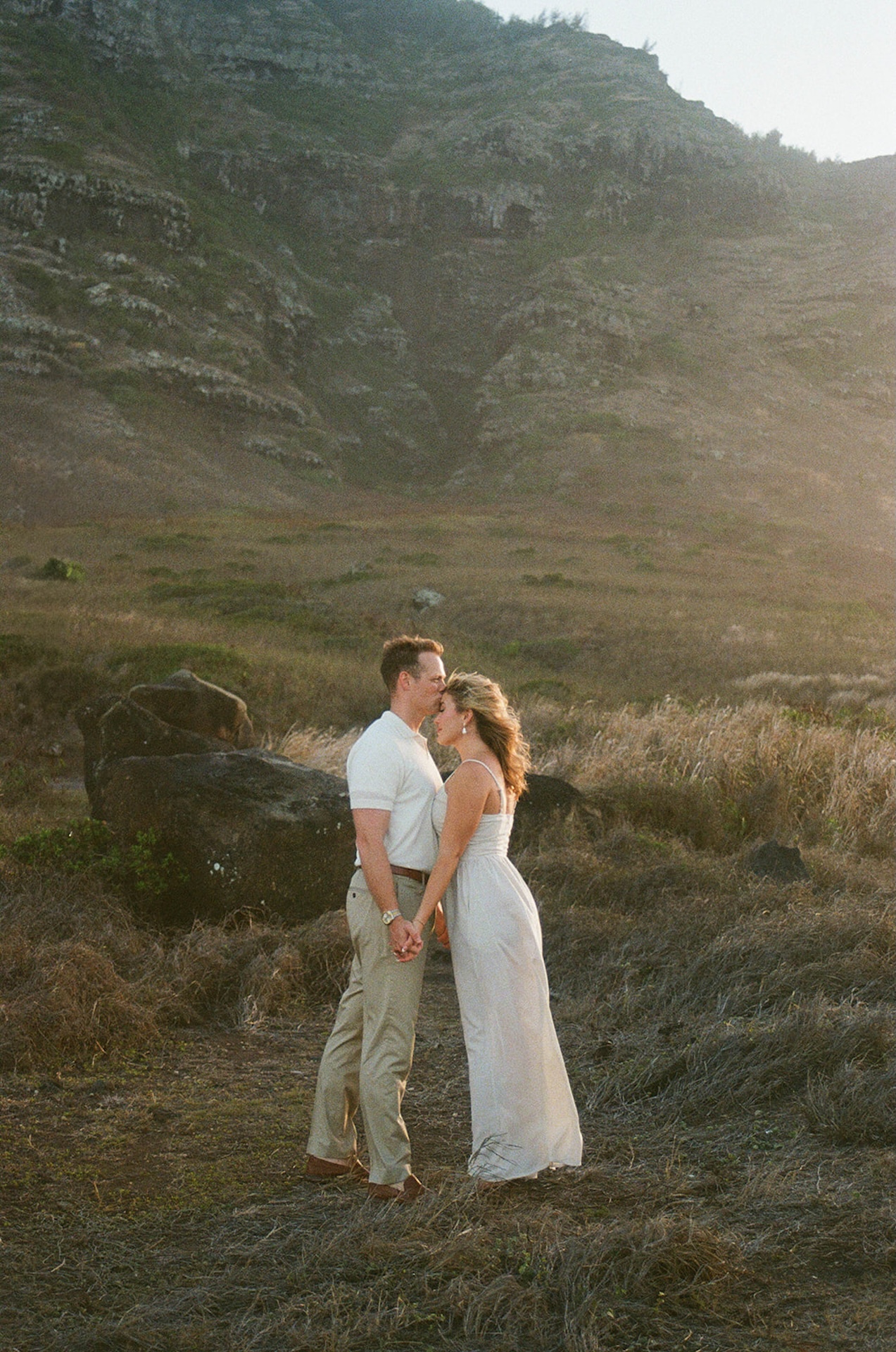 A quiet, romantic moment as the couple stands close together against a dramatic hillside backdrop.